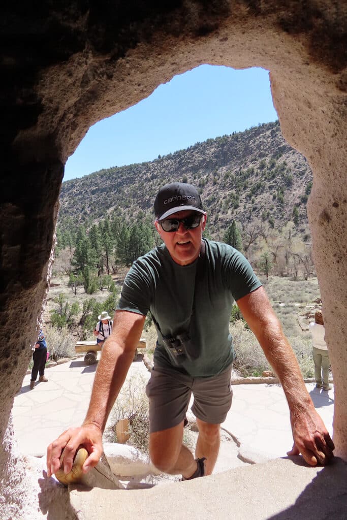 Man in rock hole opening with valley behind.