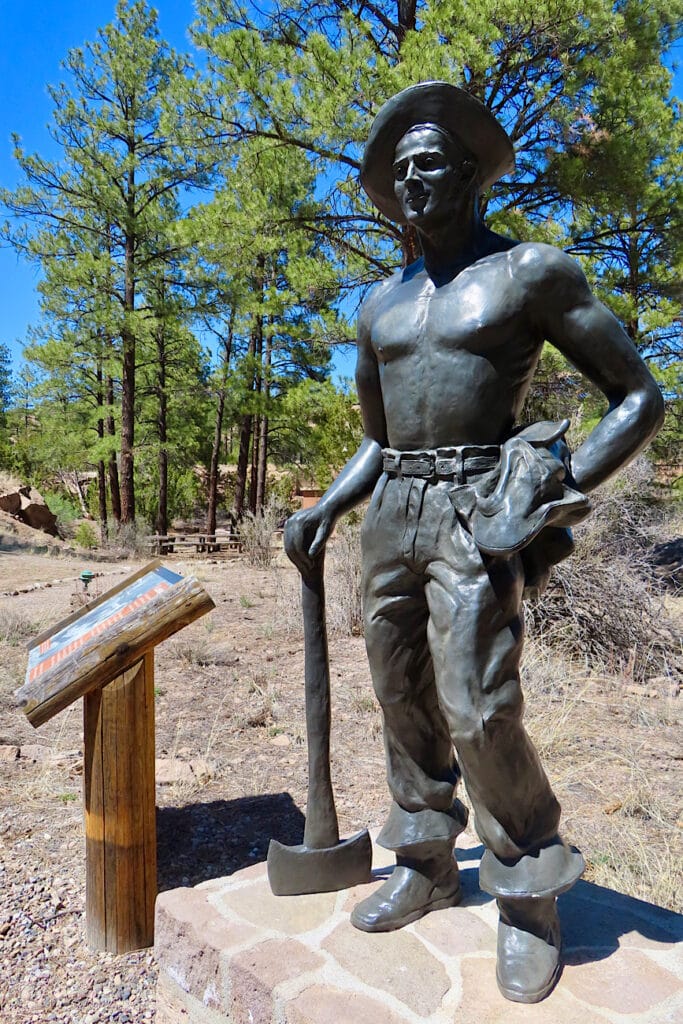 Bronze statue of young man wearing hat standing with an axe by his side.