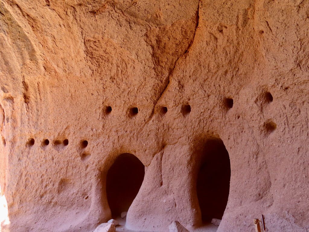 Rock wall with two large holes surrounded by multiple small holes.