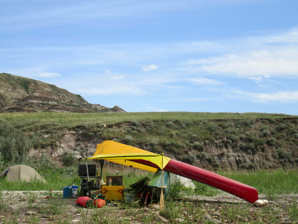 Red and green canoes resting on each other with yellow tarp above. 