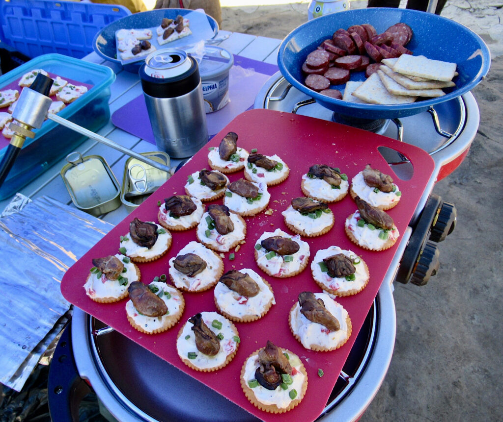 Crackers with cream cheese topped with oysters laid out on red cutting board.