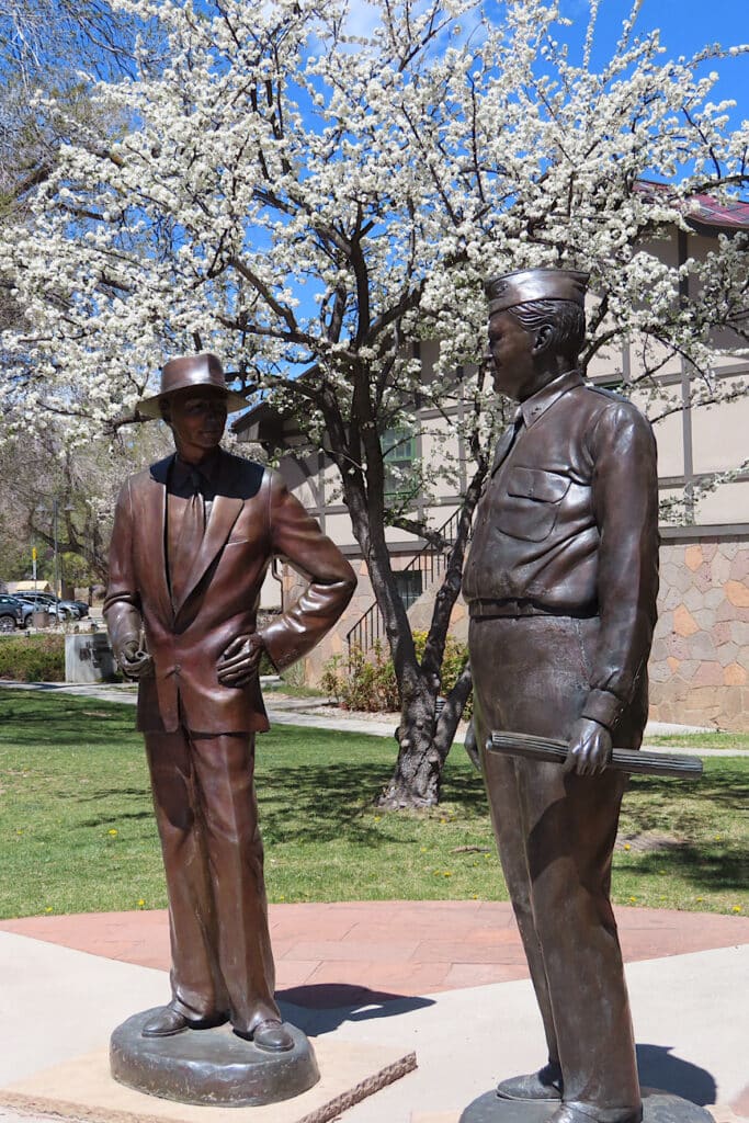 Statue of a man in hat and suit beside statue of an army man in full uniform.