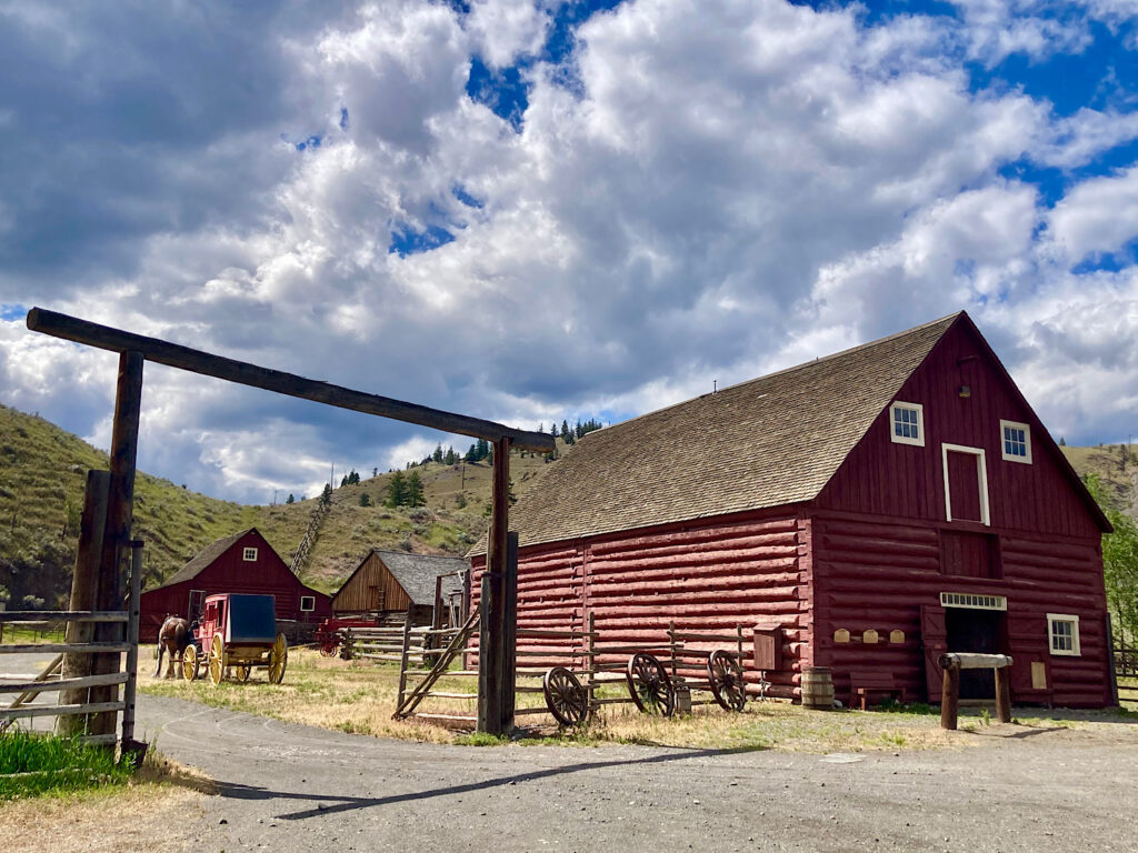Old reddish-brown painted log barn with white trim and wooden entrance gateway.