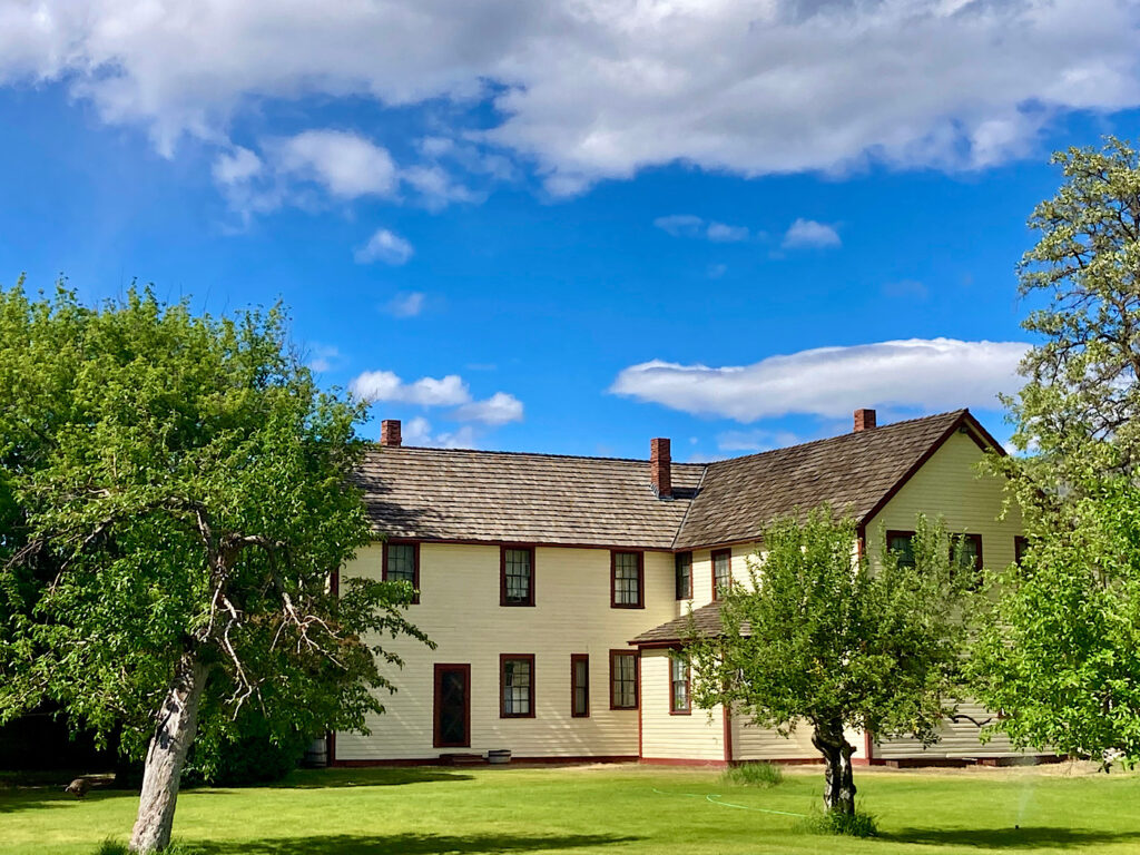 Large yellow two story building with green lawn and trees in front.
