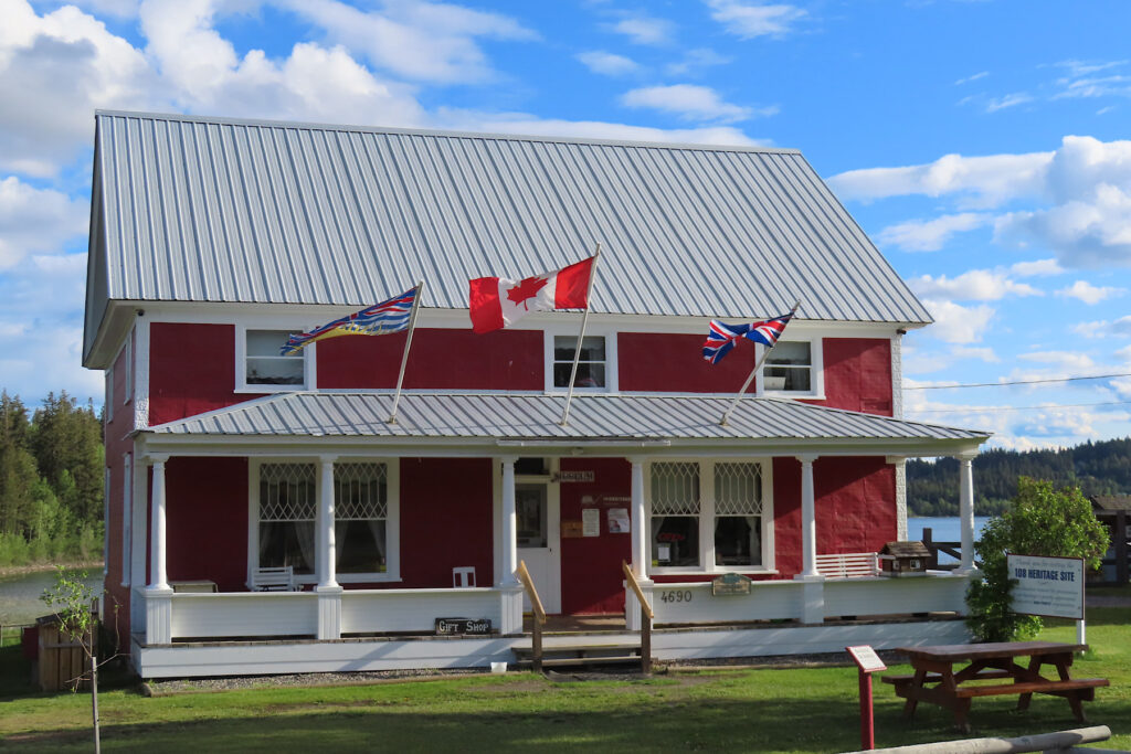 Red house with white roofed veranda holding Canadian, BC and British flags.