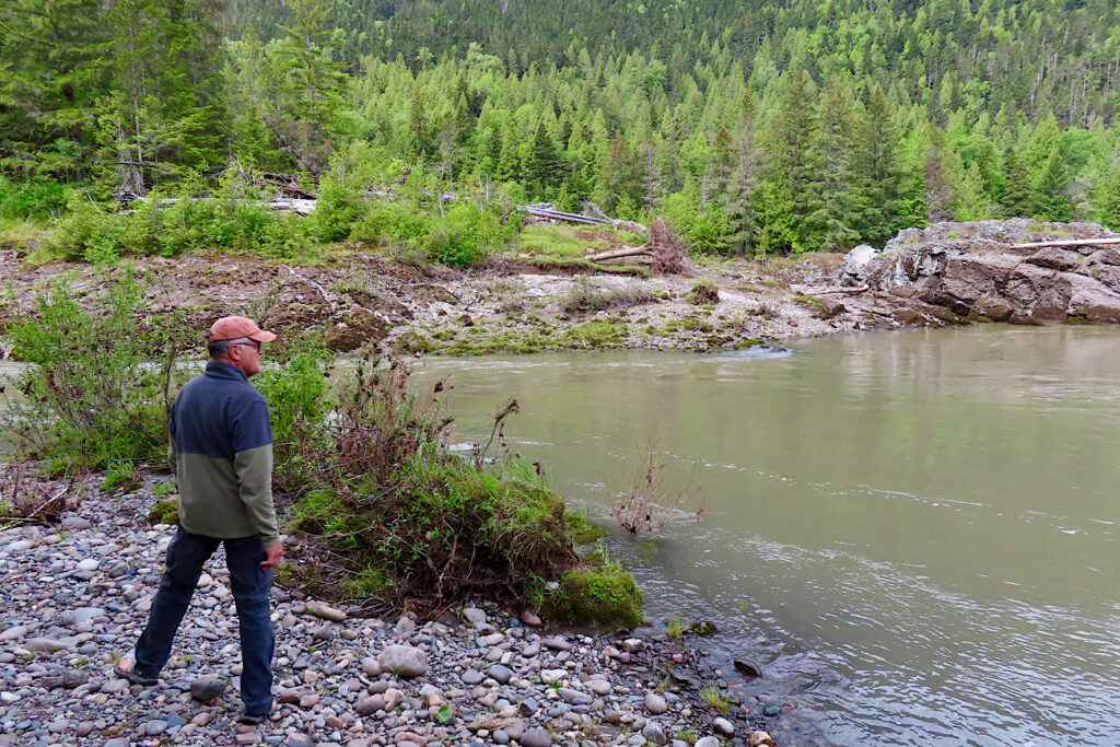 Man standing on rocky beach by water's edge.