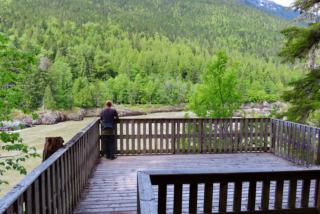 Man standing on wooden viewing platform above a river.
