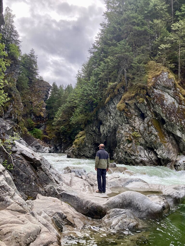 Man stand on waterworn rock beside creek running through small canyon.