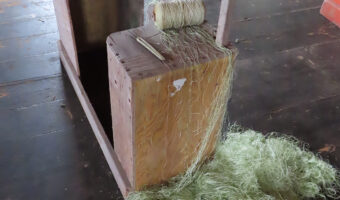 Pile of green net below block of wood with roll of thread on top.