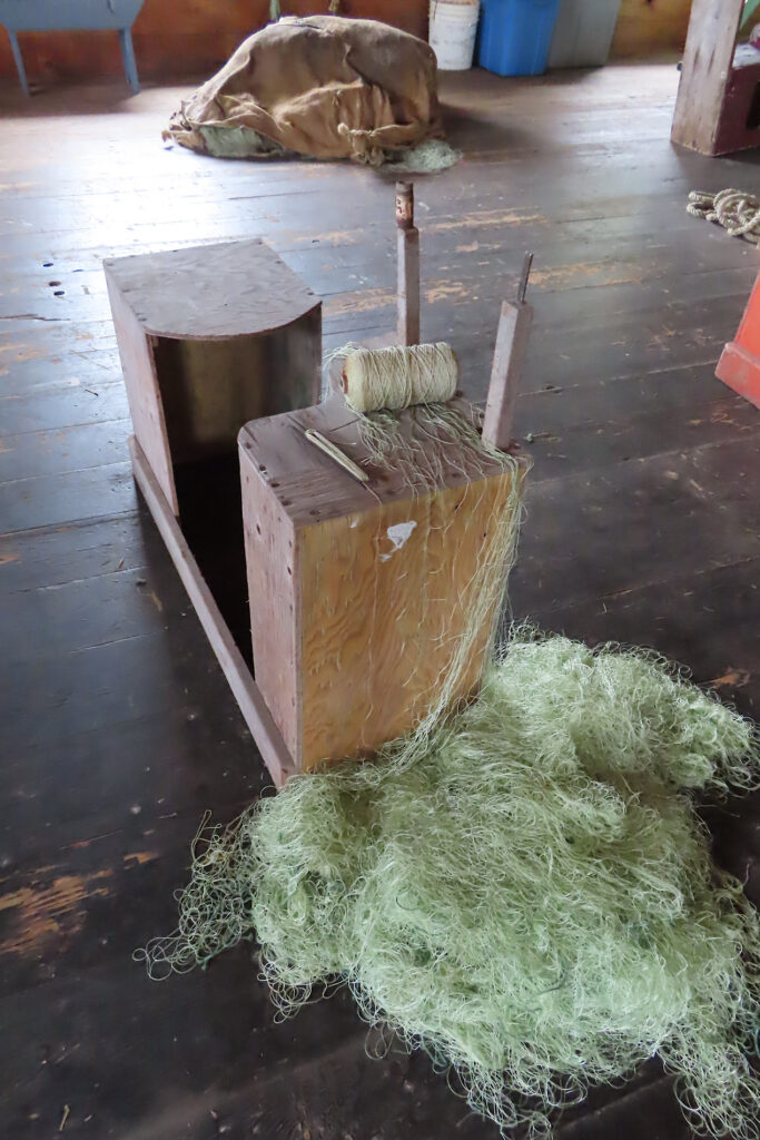 Pile of green net below block of wood with roll of thread on top.