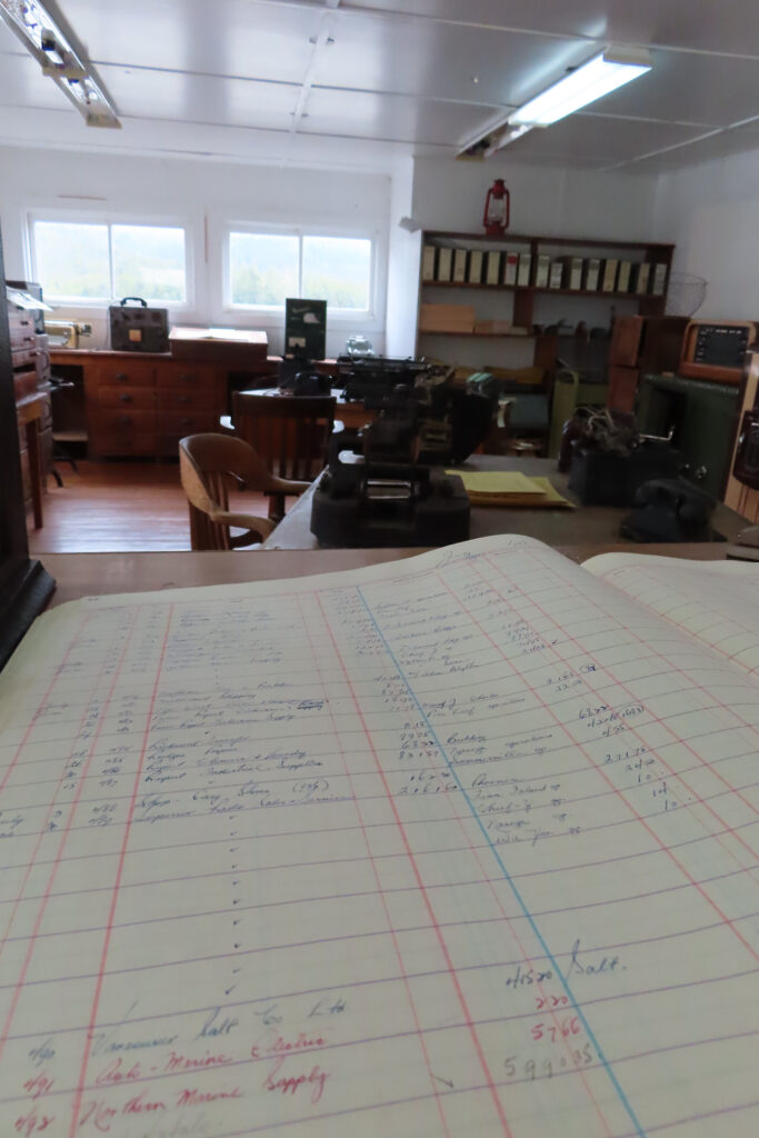 Old fashioned log book open to show entries with office behind.