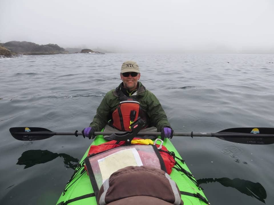 Man in kayak on ocean with fog in background.