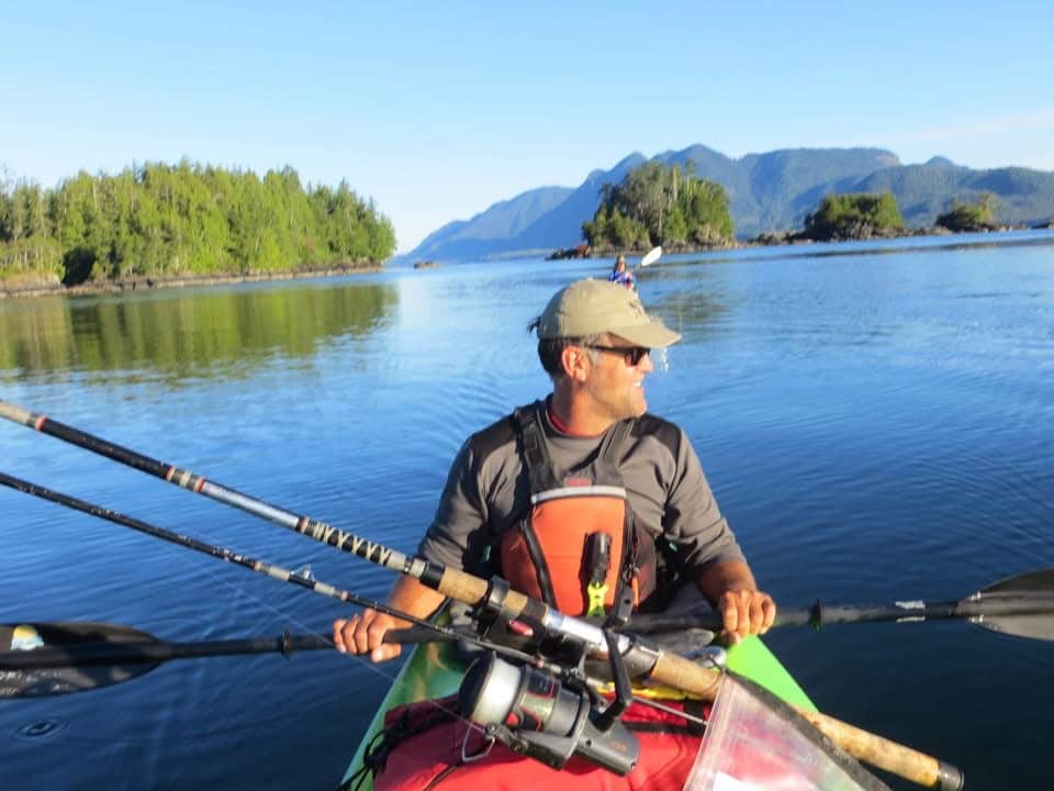 Man in kayak with fishing poles on ocean with small islands in background.