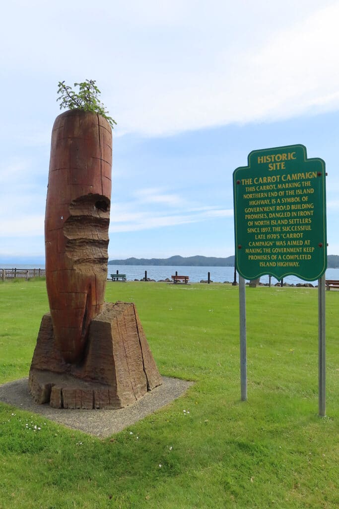Wooden carrot statue beside green interpretive sign.