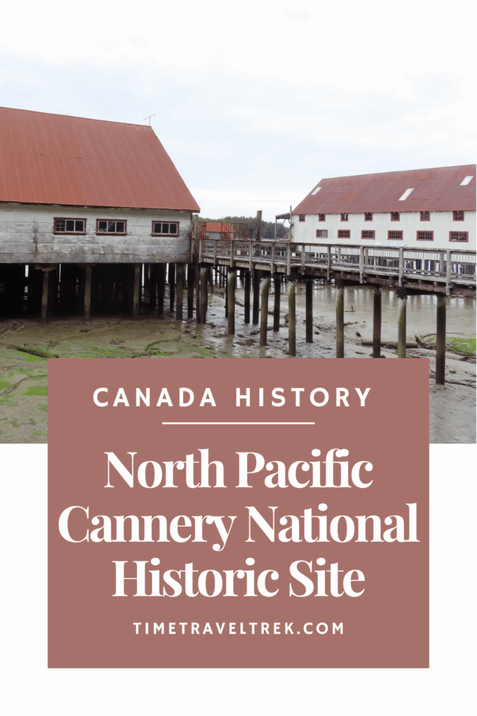 Wooden boardwalk and peeling, white-painted buildings with reddish brown roofs on stilts above tidal flats. White text in brown box reads: Canada History. North Pacific Cannery National Historic Site. TimeTravelTrek.com.