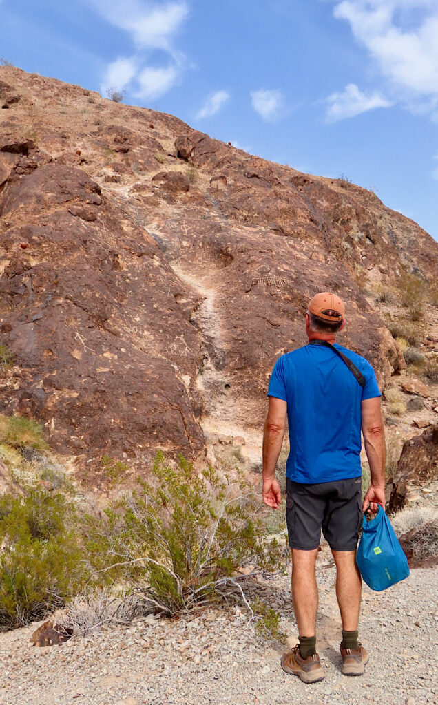 Man standing in front of large rock wall covered in rock art.
