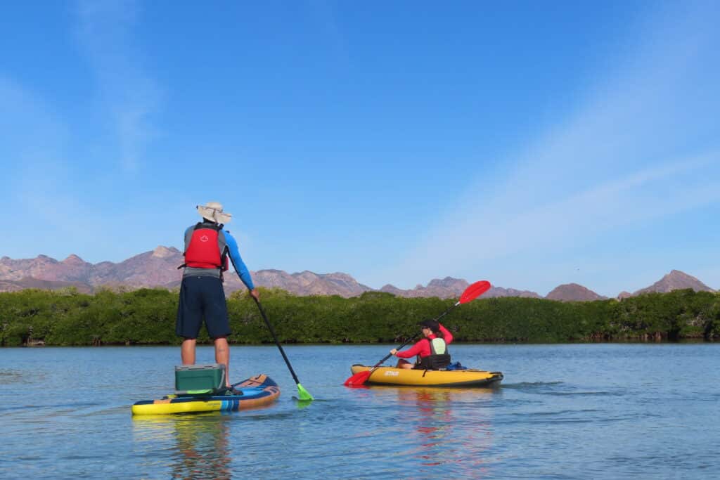 Man on standup paddleboard and woman in kayak on flat water.