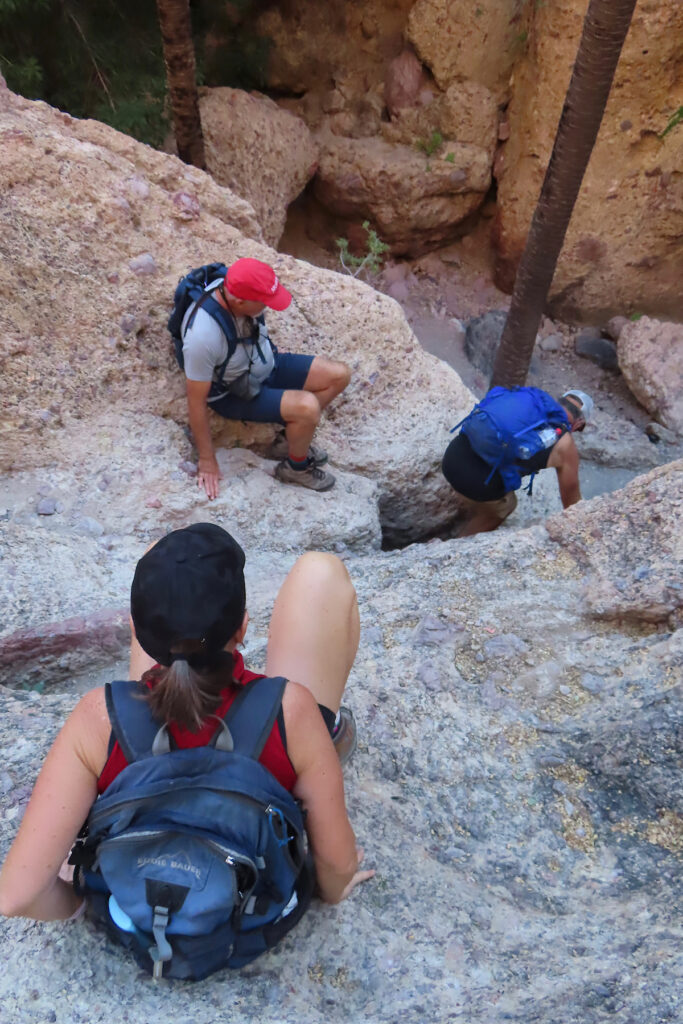 Two men and a woman scrambling down a rock face.