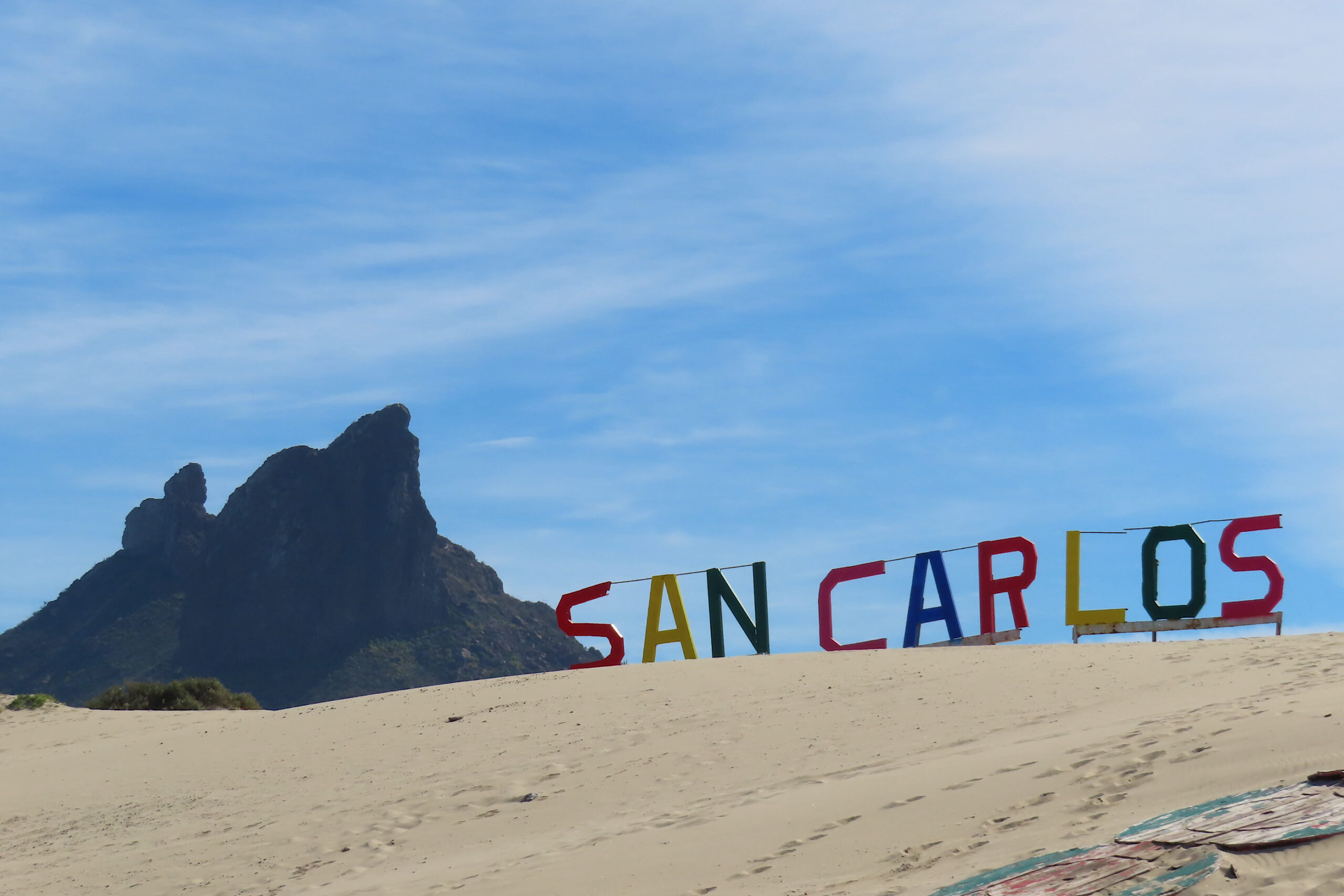 San Carlos in large primary coloured blocks on top of sand dune with dark peak in background.