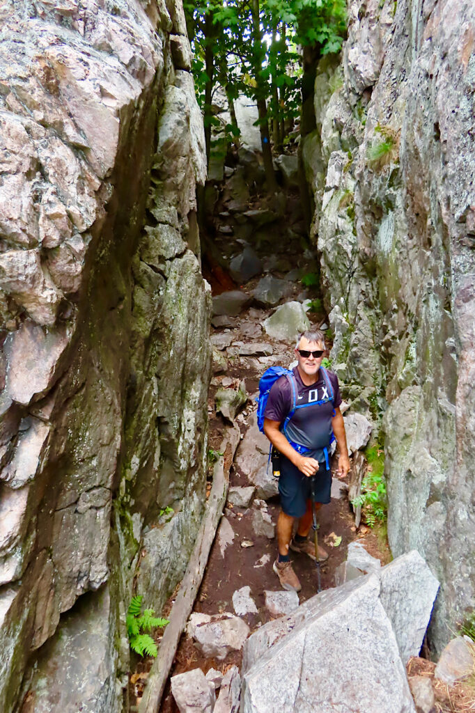 Man in shorts and wearing backpack standing in middle of path going between rock walls.