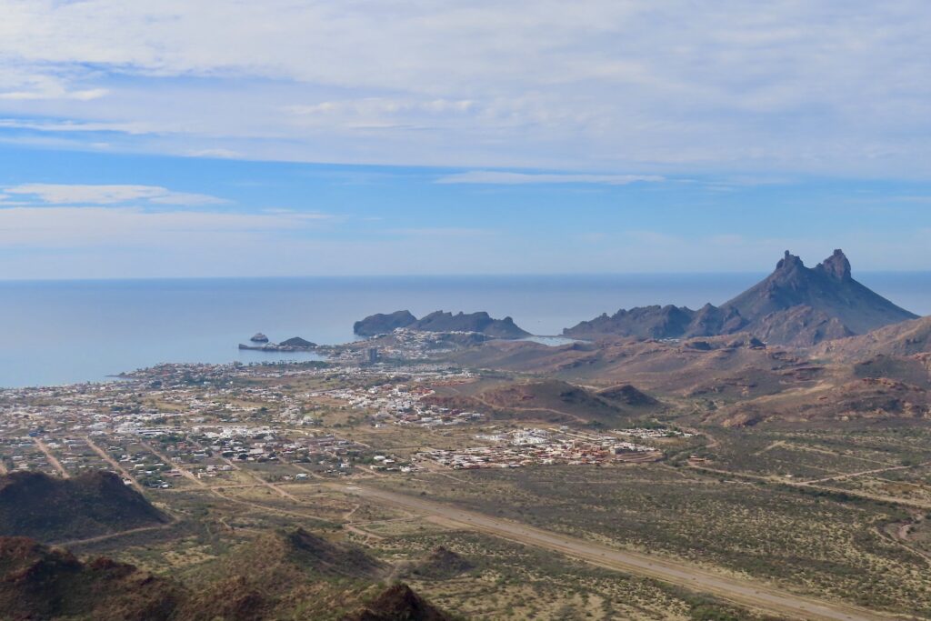 Distinct twin peak mountain, ocean and town on sea shore.