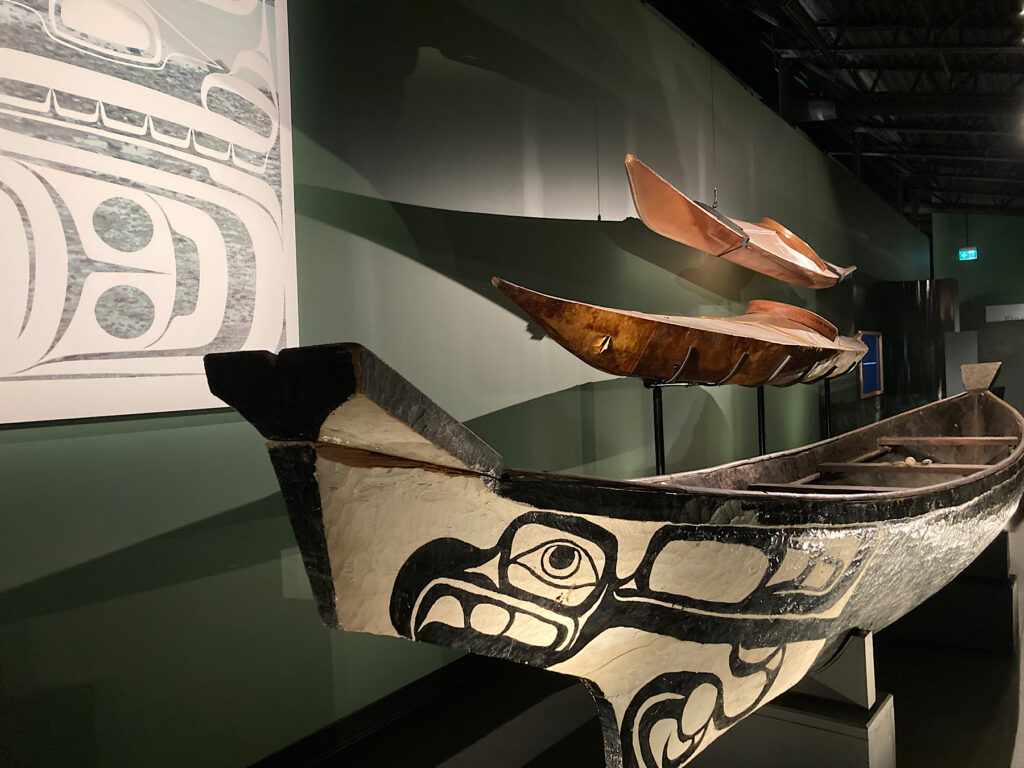 Large wooden canoe with painted indigenous art in museum display.