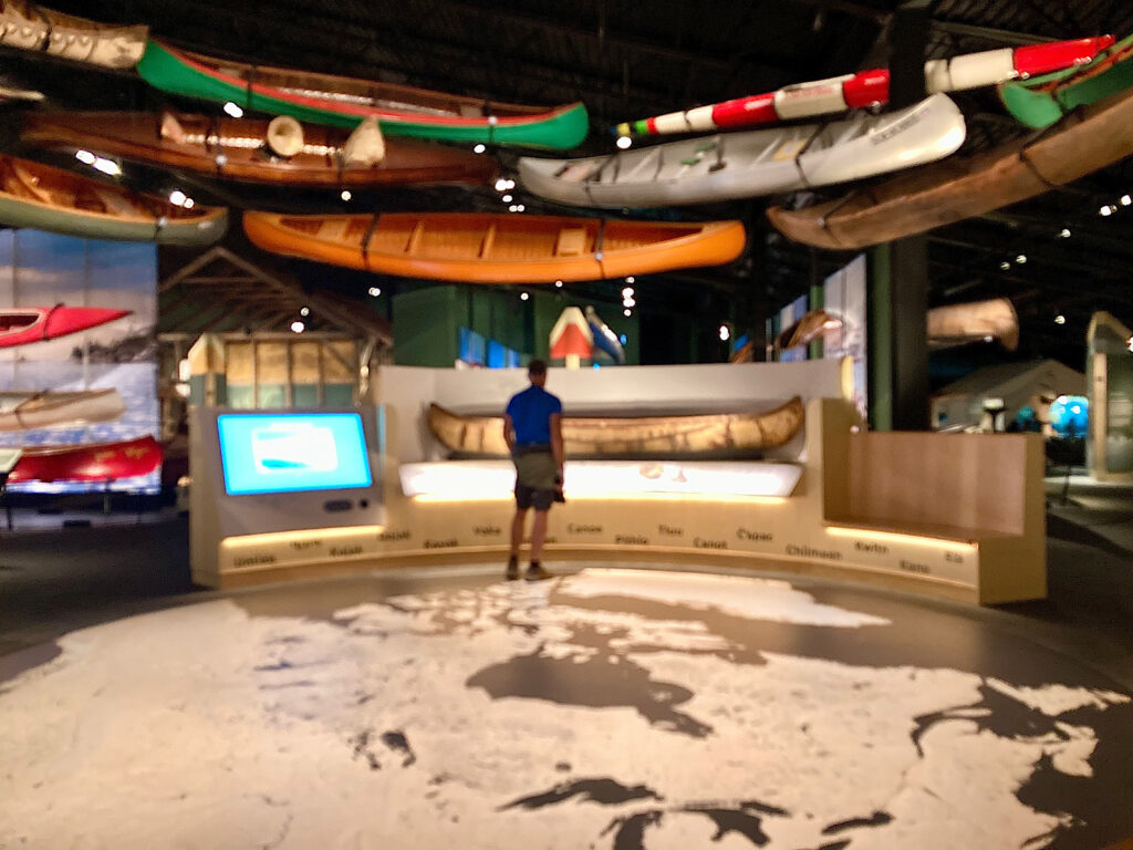 Man standing on floor map with canoes suspended overhead.