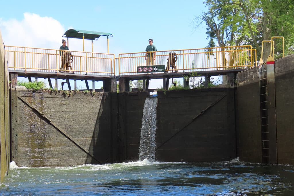 Water pouring over wooden gates with two people standing on top to one side.