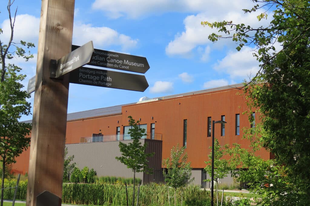 Signpost pointing to campground, museum and locks with large brown building in background.