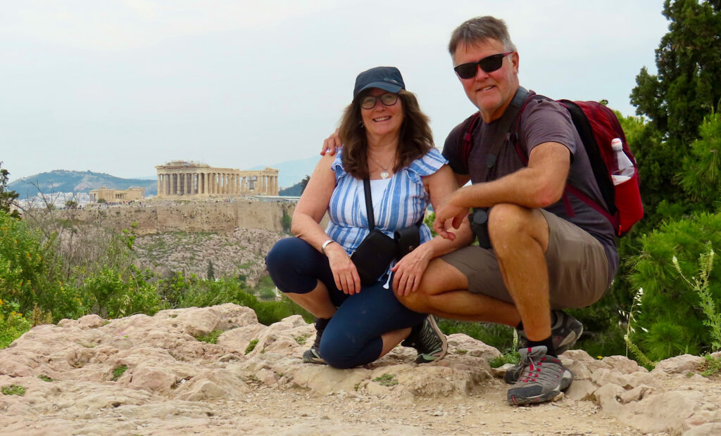 Man and woman crouched for photo with Greek monuments in background.