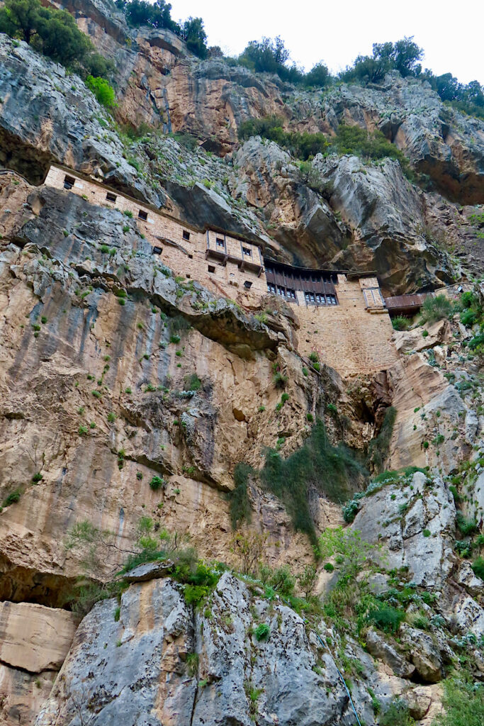 Stone building high on rugged cliff wall.