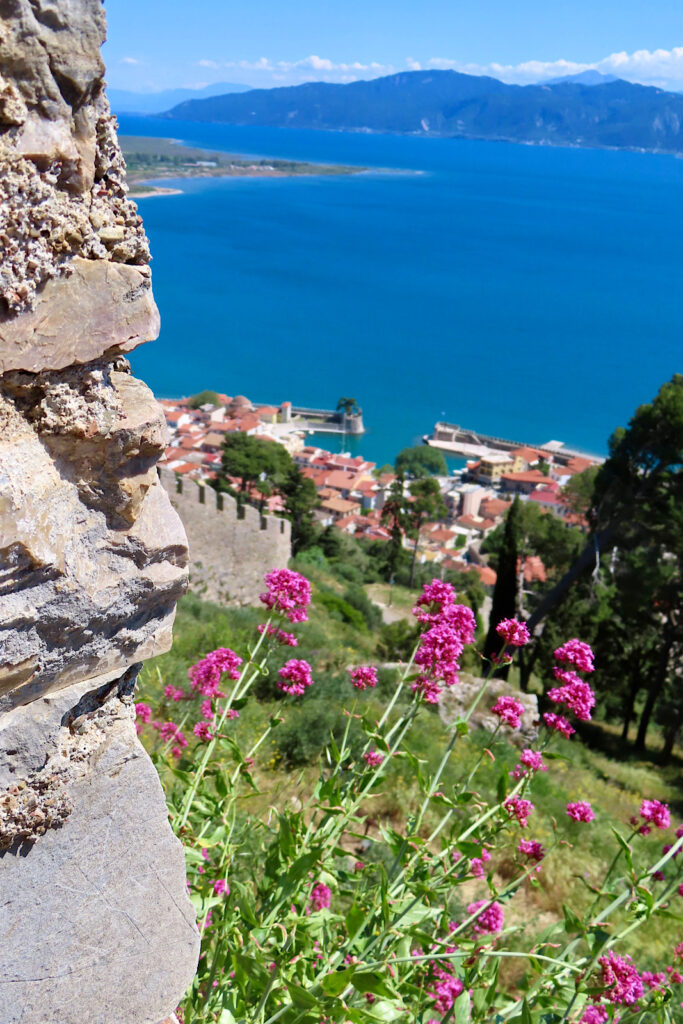 View from stone wall high above small port and large body of water.