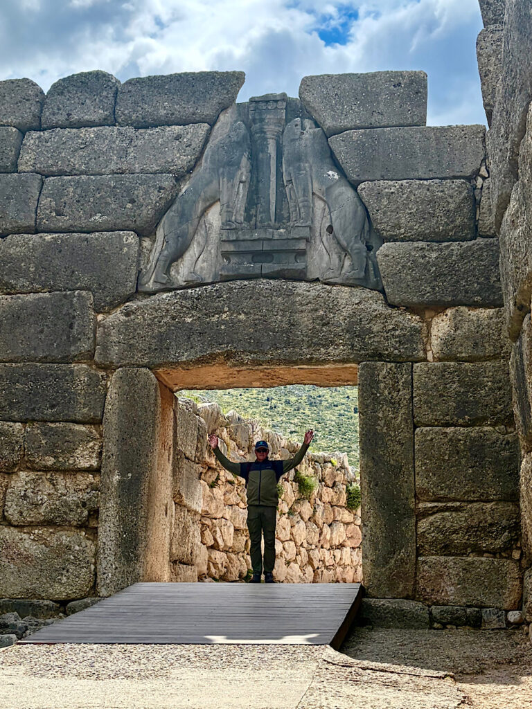 Man standing under stone archway with carved lions overhead.