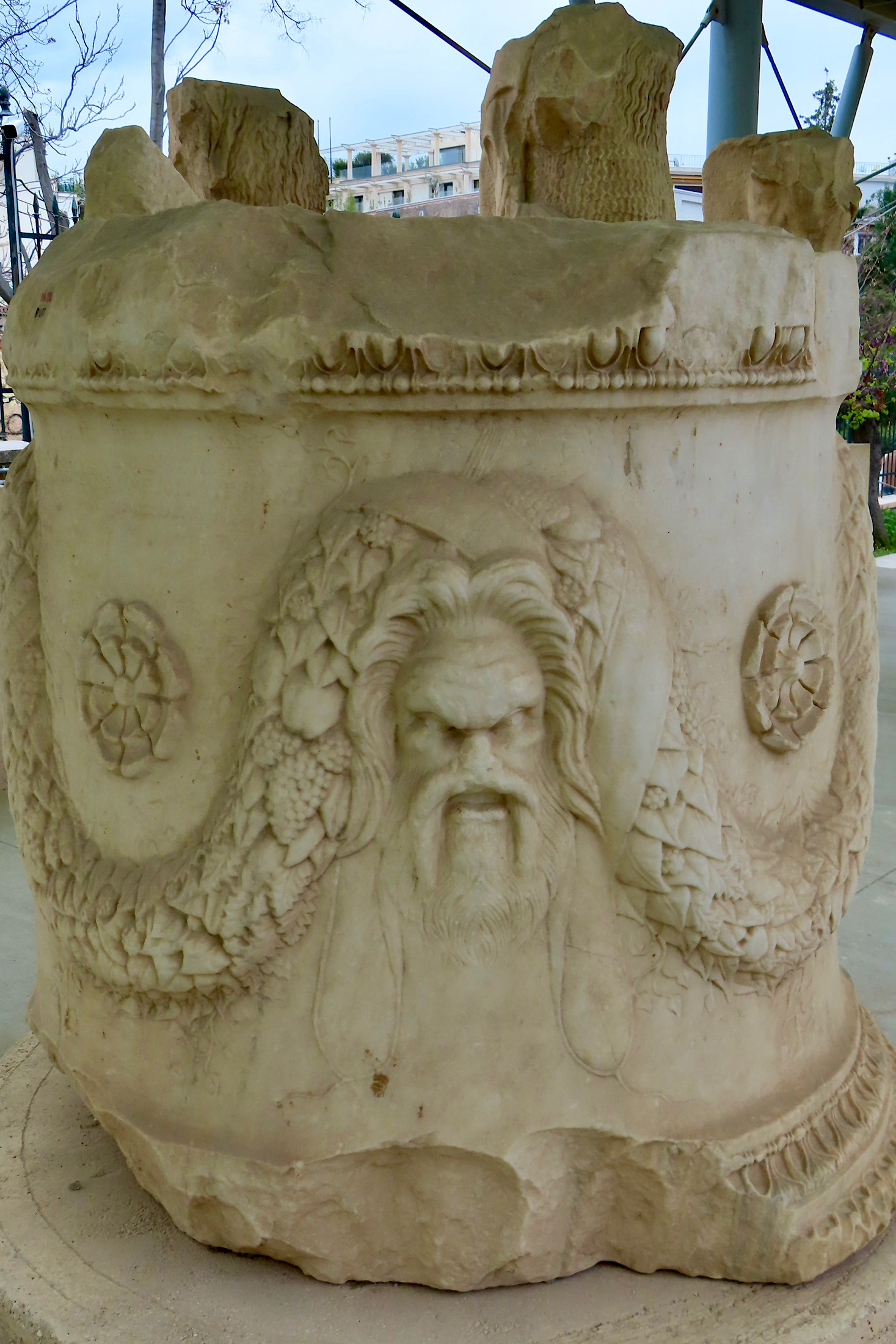 Round marble statue with image of a man and grape vines carved along side.