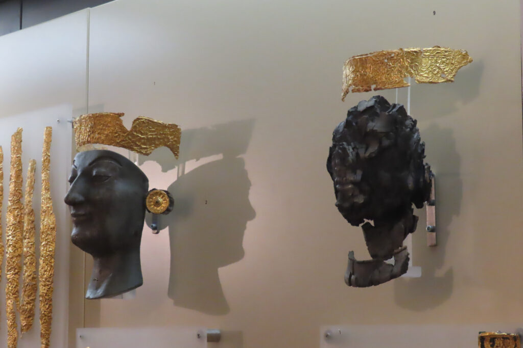 Blackish statues of heads with gold headbands in display case.