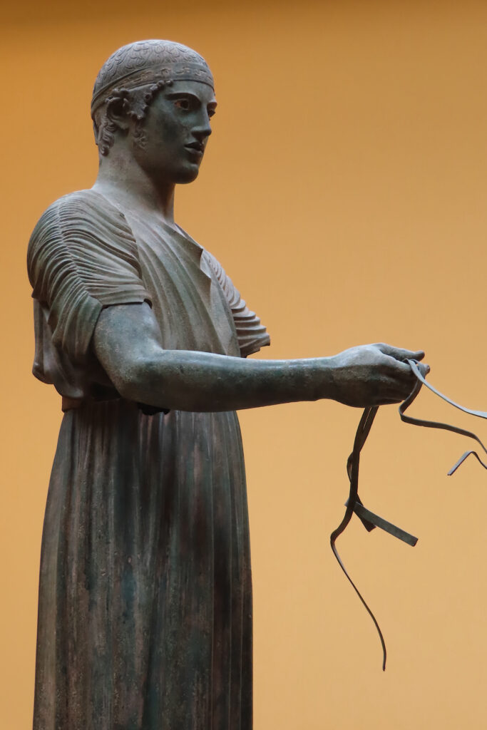 Metal statue of man in historic robe holding metal strips in hand.