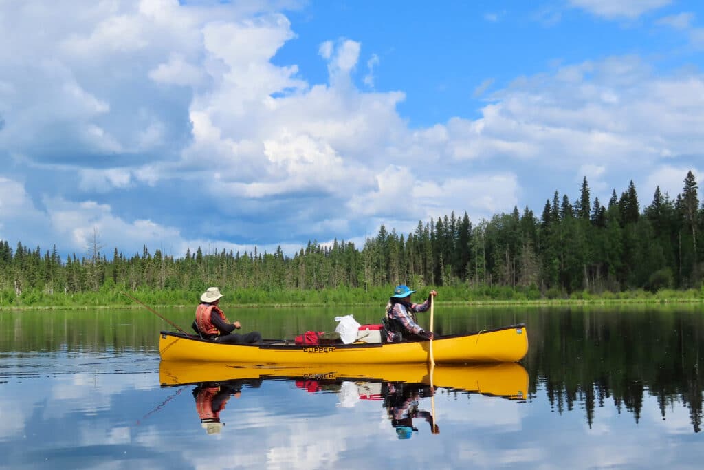 Yellow canoe reflecting on water under partially cloudy sky.