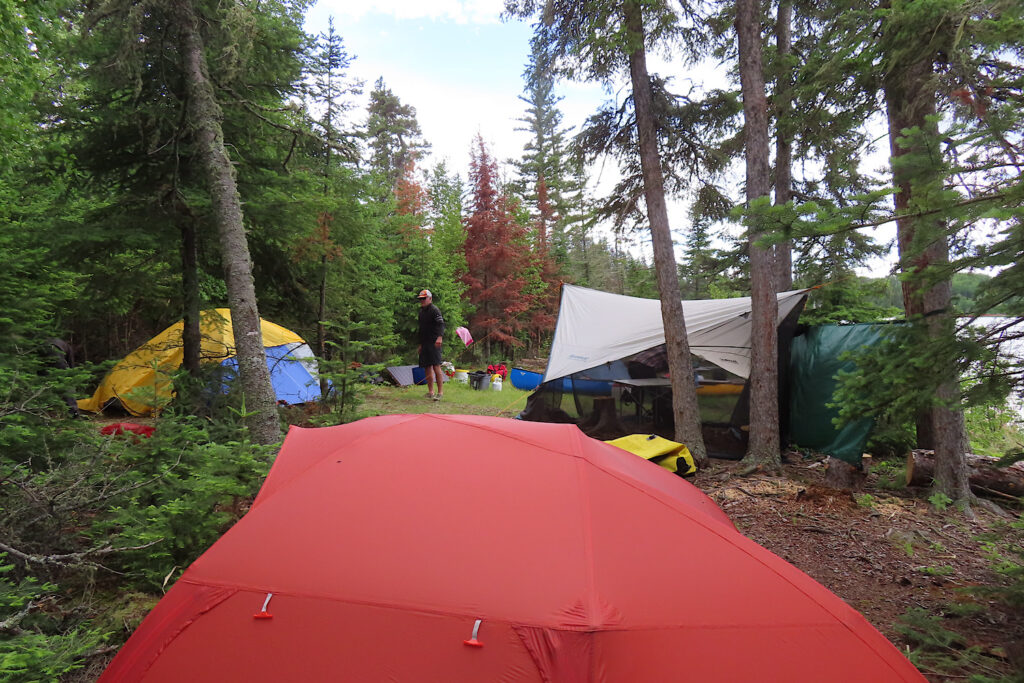 Red and yellow tents and bug tarp shelter set up in trees.