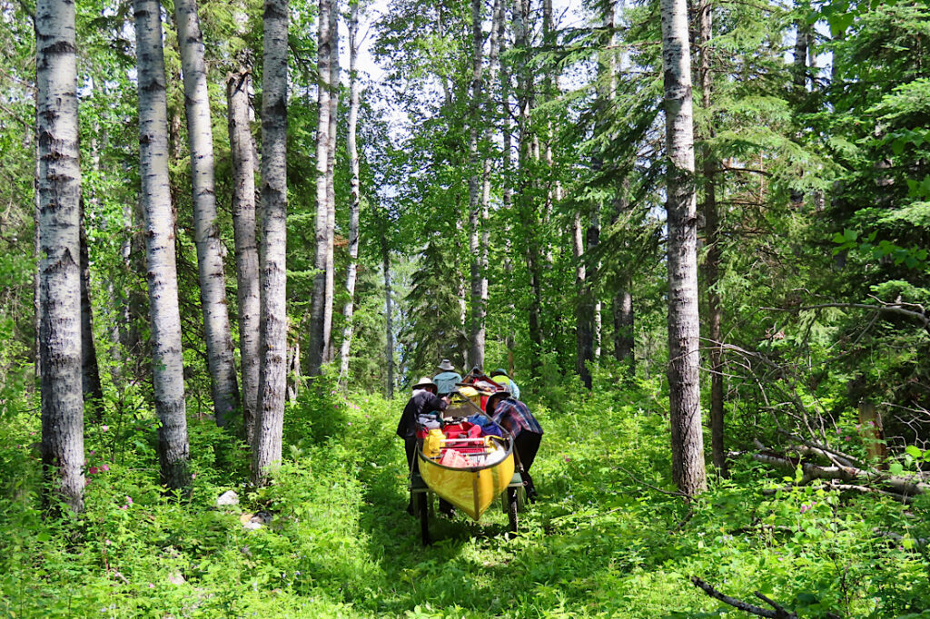 Man and woman pushing yellow canoe on a cart through a wooded path.