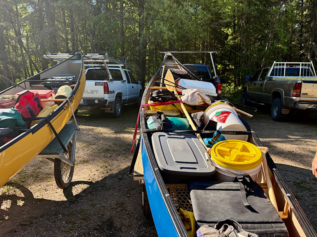 Two loaded canoes on carts in front of trucks.