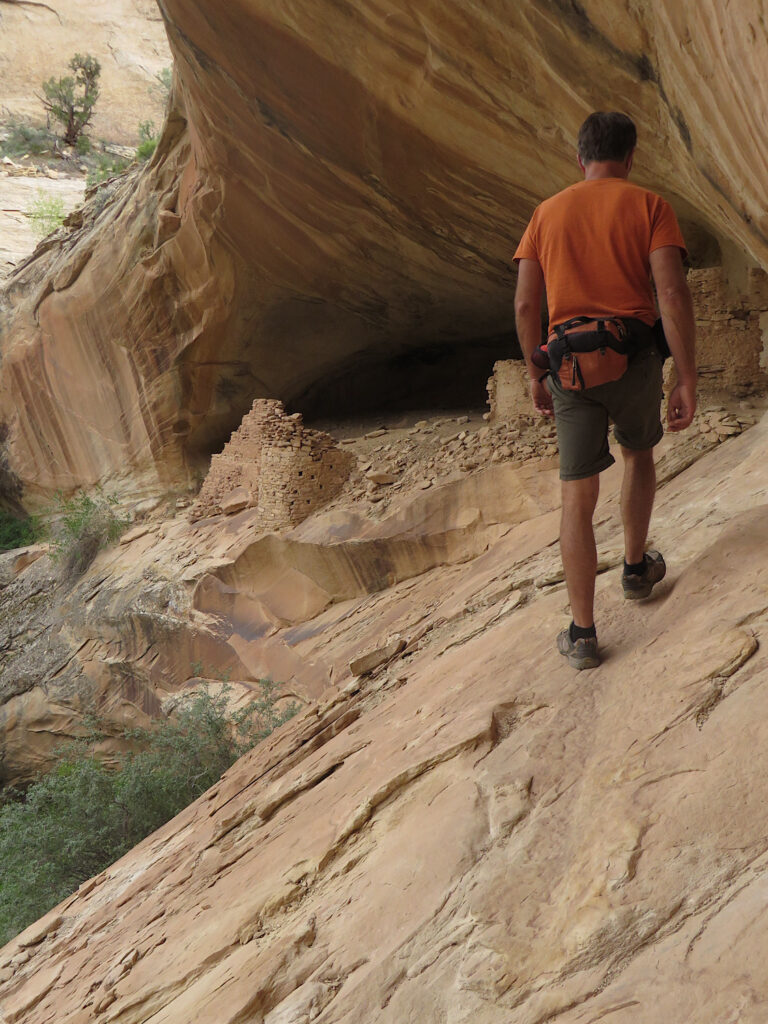 Man walking on brown sloping rock towards a stacked rock structure.