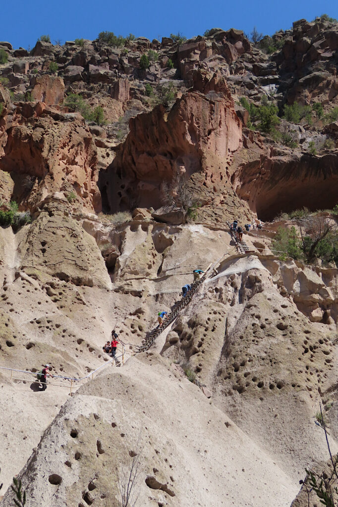 Distant photo of rugged rocky cliff with people climbing several ladders.