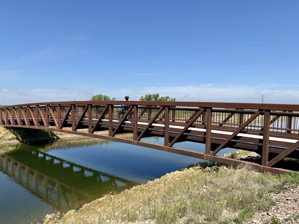 Woman on bicycle riding across metal bridge over a canal.